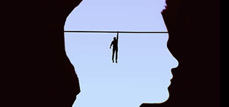 Silhouette of figure hanging from tightrope